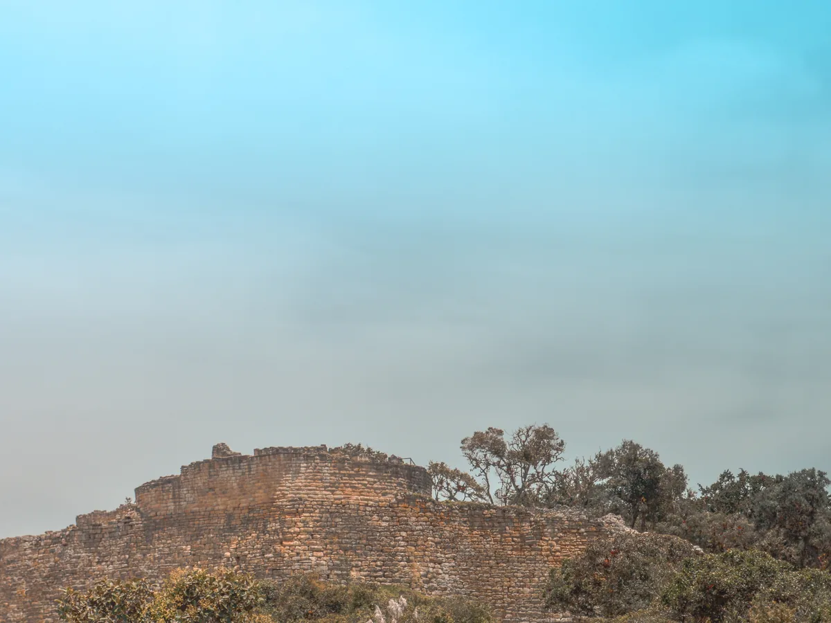 Kuélap's perimeter wall seen from a distance along the cloud-forest ridge, low stone ramparts silhouetted against the sky with trees growing along the ridgeline